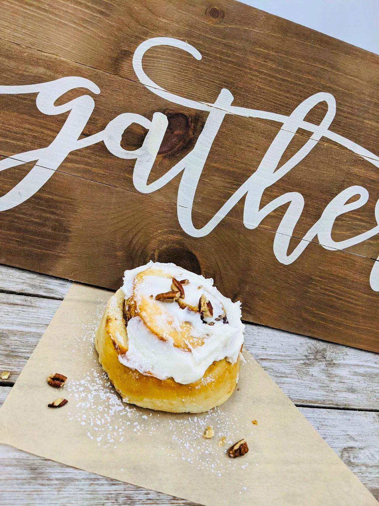 Cinnamon bun on white-washed wood with the word Gather behind it